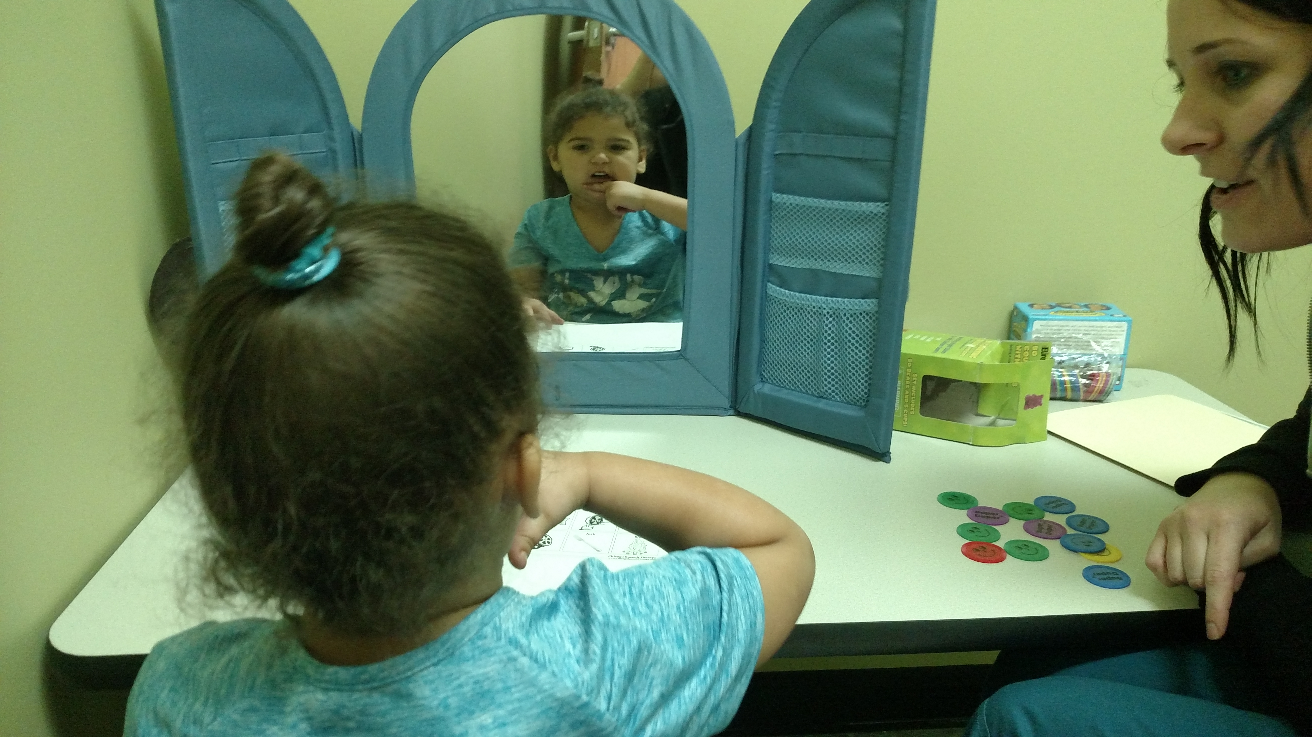 Therapist and girl practicing speech in a child's mirror