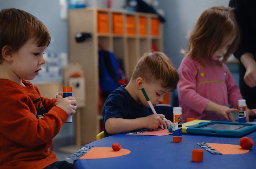 Children at a table doing crafts with glue, markers, and construction paper